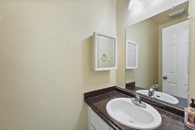 bathroom featuring visible vents, a textured wall, and vanity