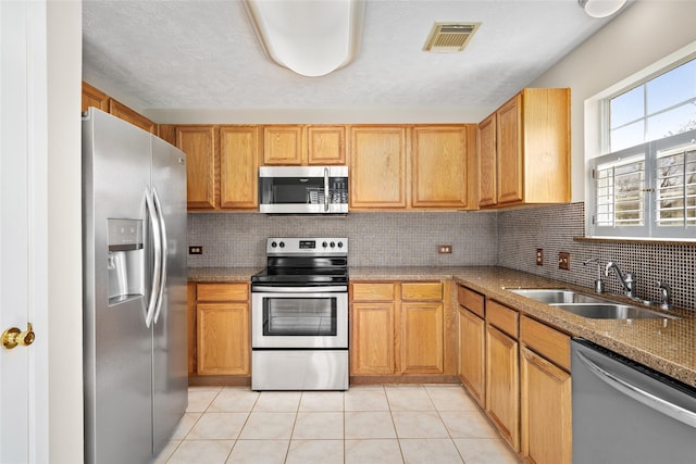 kitchen with light tile patterned floors, a sink, visible vents, appliances with stainless steel finishes, and decorative backsplash