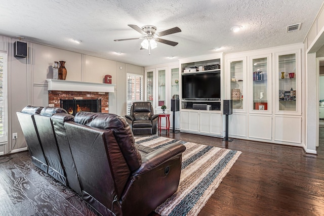 living area with visible vents, a fireplace, ceiling fan, dark wood-type flooring, and a textured ceiling