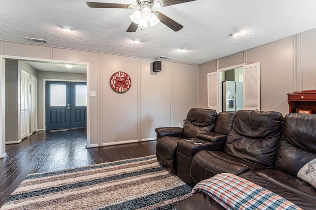 living area featuring a decorative wall, visible vents, dark wood-style flooring, and ceiling fan