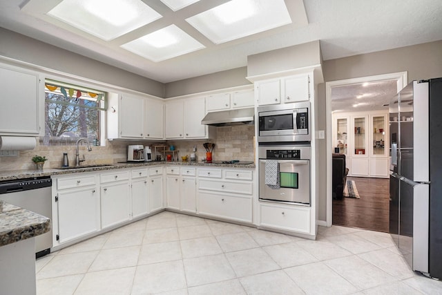 kitchen with a sink, white cabinets, under cabinet range hood, appliances with stainless steel finishes, and backsplash