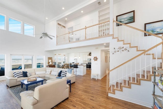 living room with visible vents, light wood-style floors, ceiling fan, baseboards, and stairs