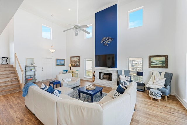 living area with stairs, a fireplace, wood finished floors, and a ceiling fan