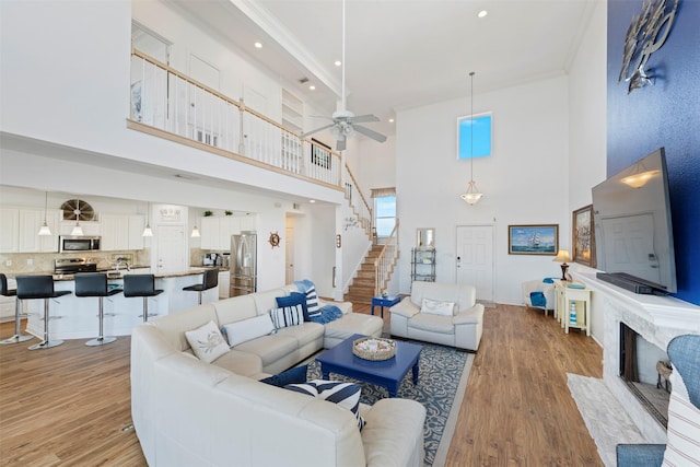 living area featuring a fireplace, crown molding, light wood-style flooring, stairway, and a ceiling fan