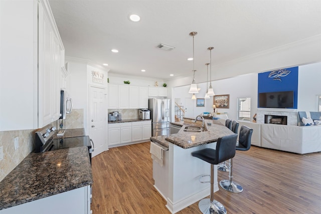 kitchen with visible vents, white cabinets, appliances with stainless steel finishes, wood finished floors, and a kitchen bar