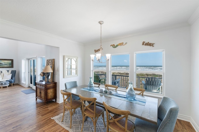 dining area with a water view, an inviting chandelier, ornamental molding, wood finished floors, and baseboards