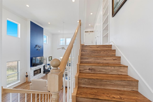 stairs featuring recessed lighting, a fireplace, wood finished floors, a towering ceiling, and crown molding