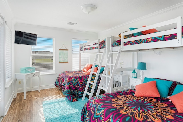 bedroom with baseboards, visible vents, ornamental molding, and wood finished floors