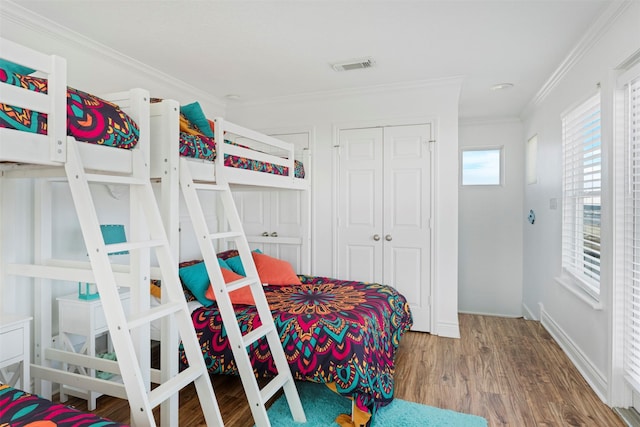 bedroom with baseboards, visible vents, wood finished floors, crown molding, and a closet