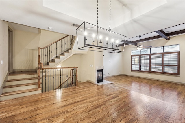 unfurnished living room featuring a fireplace, wood finished floors, visible vents, baseboards, and beamed ceiling