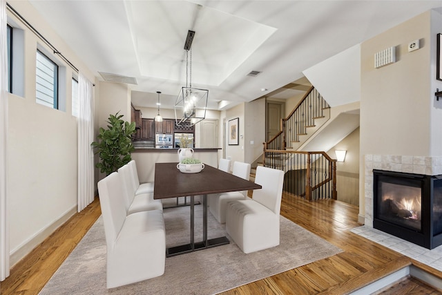 dining room with stairway, light wood-style flooring, visible vents, and a tray ceiling