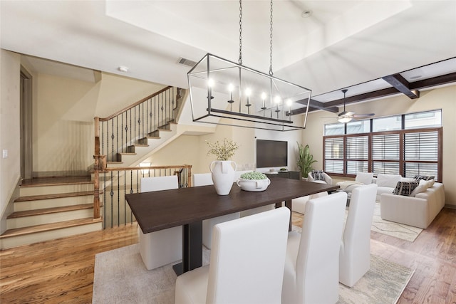 dining space featuring beam ceiling, visible vents, stairway, wood finished floors, and ceiling fan with notable chandelier