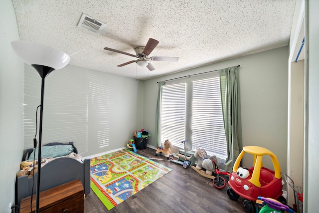 recreation room featuring visible vents, baseboards, ceiling fan, wood finished floors, and a textured ceiling