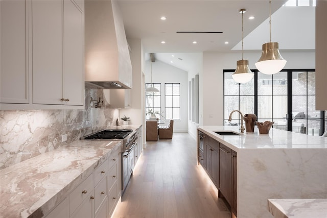 kitchen with light stone countertops, light wood-type flooring, decorative backsplash, custom exhaust hood, and a sink