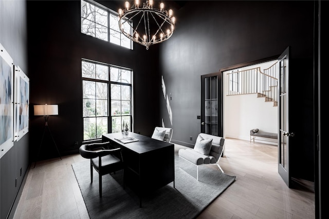 office space featuring baseboards, light wood-type flooring, a towering ceiling, and a chandelier