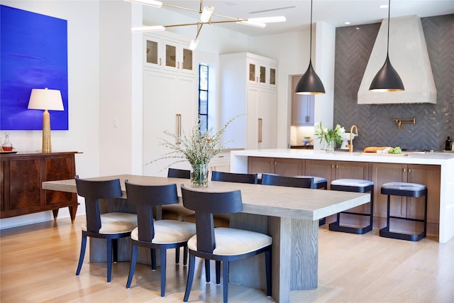 kitchen featuring backsplash, decorative light fixtures, light countertops, light wood-style flooring, and white cabinetry