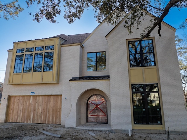 view of front of property with a standing seam roof, a garage, brick siding, and roof with shingles