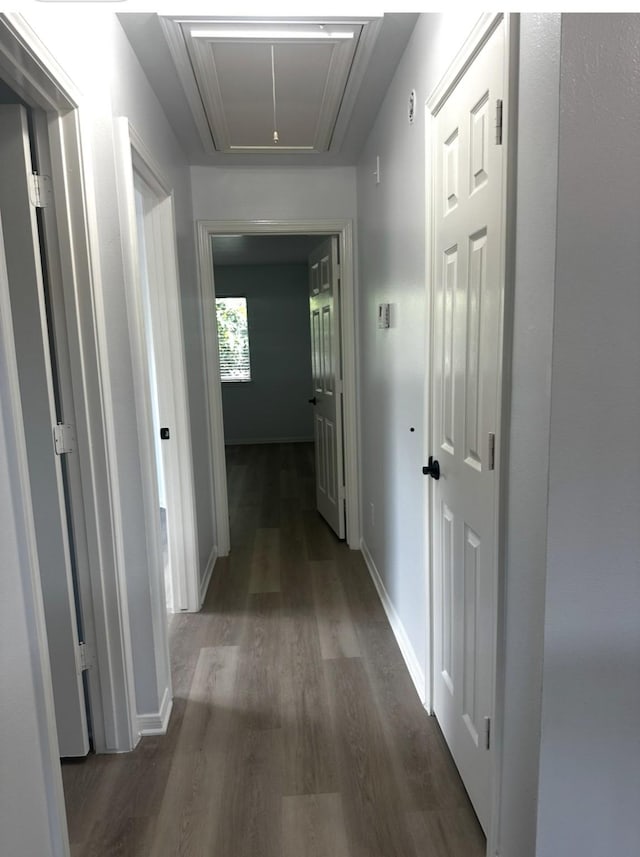 corridor featuring attic access, baseboards, and wood finished floors