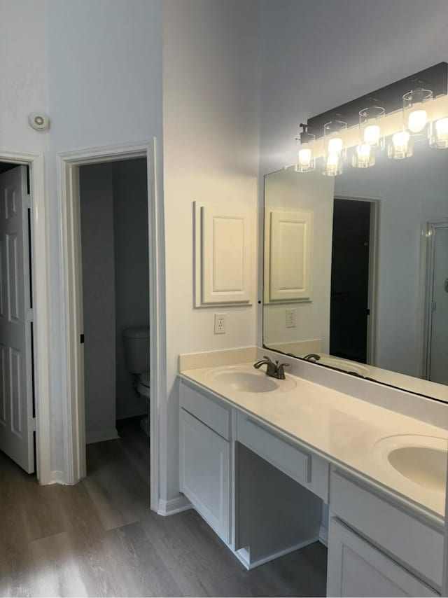 full bath with wood finished floors, a sink, toilet, and double vanity