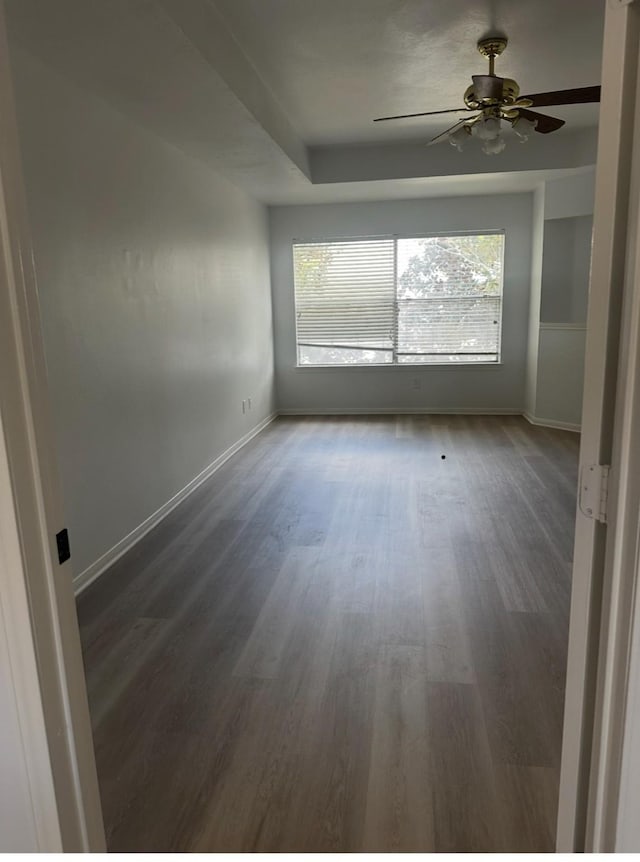 empty room featuring a tray ceiling, baseboards, ceiling fan, and wood finished floors