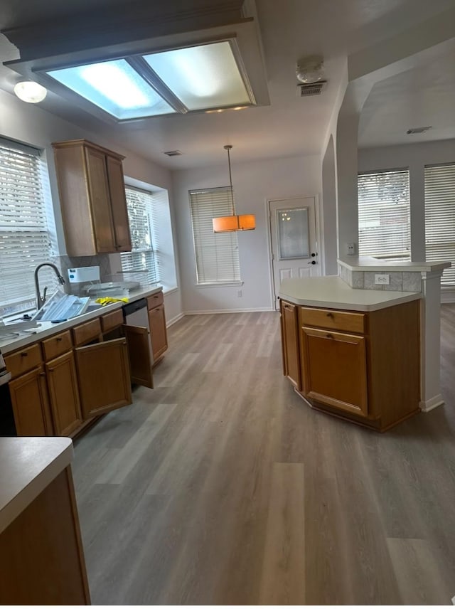 kitchen with light wood finished floors, light countertops, visible vents, brown cabinetry, and a sink