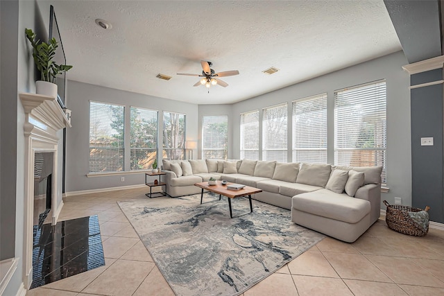 living area featuring light tile patterned floors, a textured ceiling, a fireplace with flush hearth, visible vents, and a ceiling fan