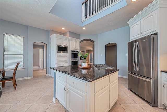 kitchen featuring light tile patterned floors, appliances with stainless steel finishes, arched walkways, and a center island