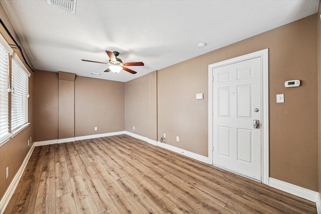 empty room with baseboards, visible vents, a ceiling fan, wood finished floors, and a textured ceiling