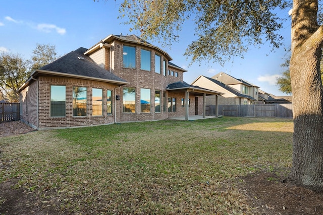 rear view of property featuring roof with shingles, brick siding, a patio, a lawn, and a fenced backyard