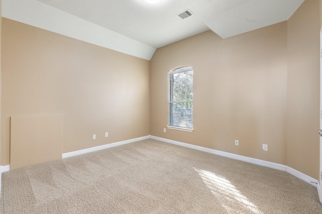 spare room with light carpet, lofted ceiling, visible vents, and baseboards