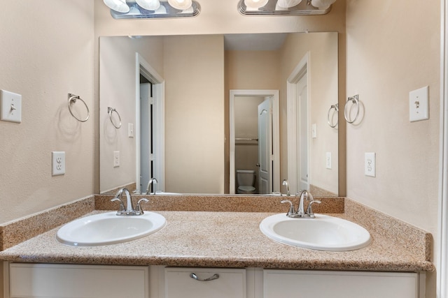 bathroom featuring double vanity, toilet, and a sink