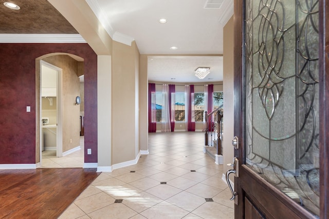 entrance foyer featuring ornamental molding, arched walkways, light tile patterned flooring, and baseboards