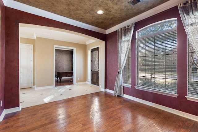 entrance foyer featuring arched walkways, visible vents, ornamental molding, wood finished floors, and baseboards