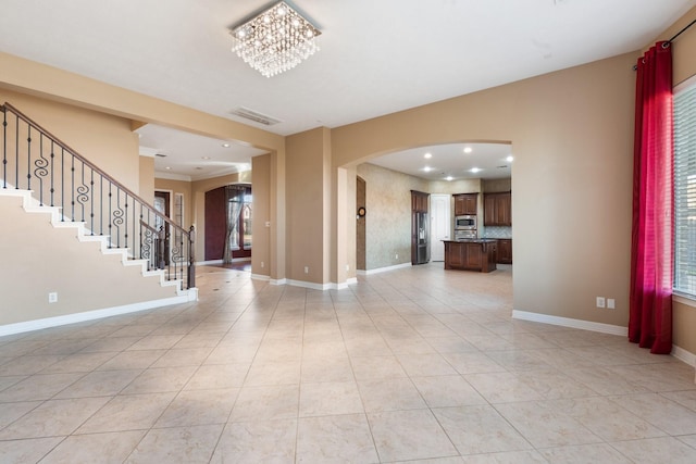 unfurnished living room featuring arched walkways, a notable chandelier, visible vents, baseboards, and stairs