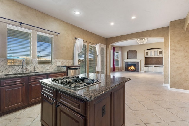 kitchen with light tile patterned floors, a warm lit fireplace, a sink, appliances with stainless steel finishes, and tasteful backsplash