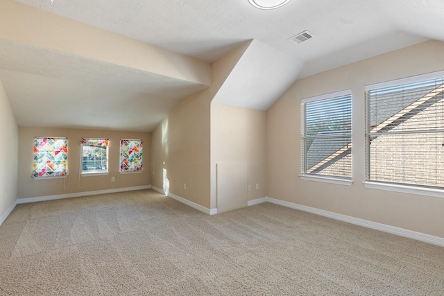 additional living space with lofted ceiling, a healthy amount of sunlight, visible vents, and baseboards