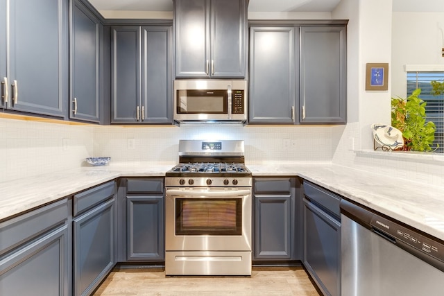 kitchen featuring backsplash, appliances with stainless steel finishes, light wood-style floors, and light stone countertops