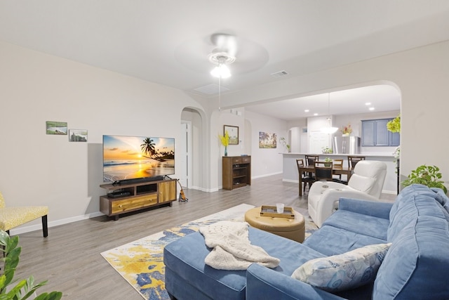 living area featuring visible vents, arched walkways, light wood finished floors, and baseboards