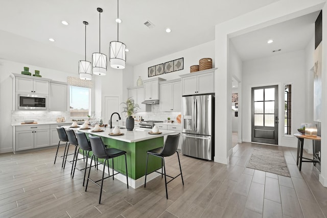 kitchen with a breakfast bar, light countertops, visible vents, appliances with stainless steel finishes, and wood tiled floor