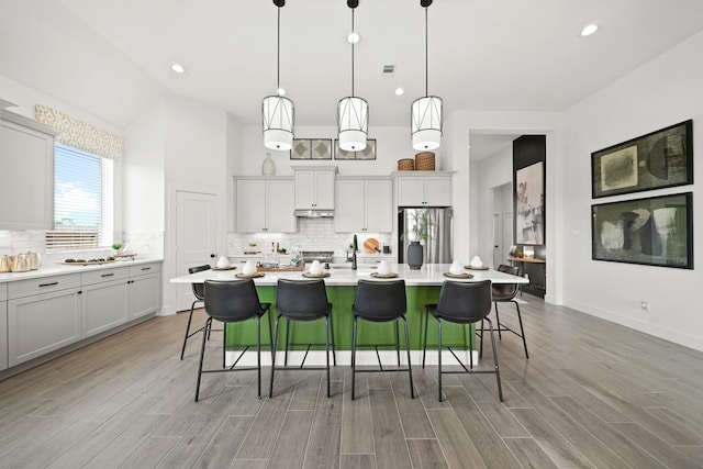 kitchen with light wood-type flooring, stainless steel fridge, tasteful backsplash, and light countertops