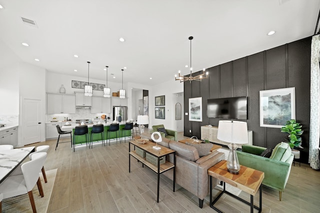 living area with visible vents, a towering ceiling, an inviting chandelier, light wood-style floors, and recessed lighting