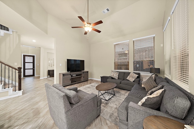 living area with a ceiling fan, baseboards, visible vents, high vaulted ceiling, and stairs