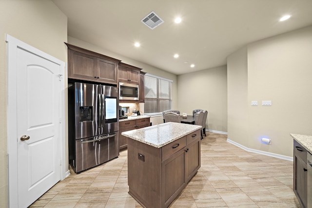 kitchen featuring light stone counters, visible vents, a kitchen island, dark brown cabinets, and appliances with stainless steel finishes