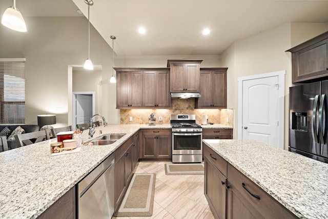 kitchen with under cabinet range hood, light stone counters, decorative backsplash, stainless steel appliances, and a sink