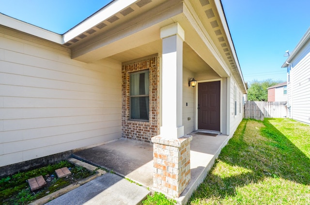 property entrance with brick siding, a lawn, and fence