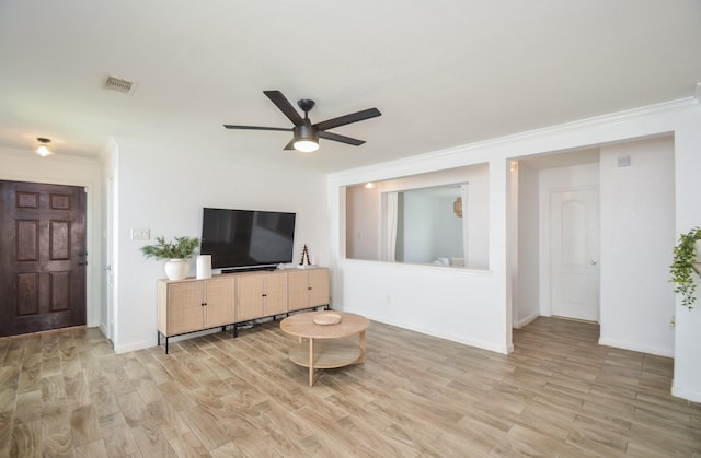 living room with light wood-type flooring, visible vents, crown molding, and baseboards