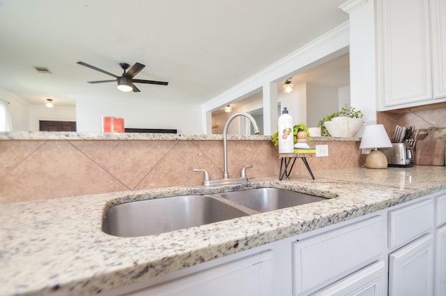 kitchen with light stone counters, tasteful backsplash, white cabinets, a sink, and ceiling fan