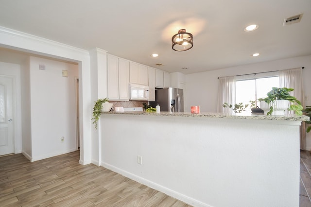 kitchen with white microwave, visible vents, light wood-style floors, stainless steel fridge with ice dispenser, and tasteful backsplash