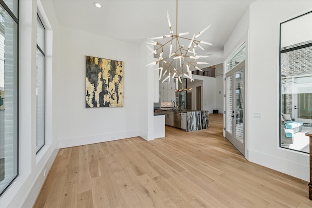 unfurnished dining area with light wood-type flooring, a high ceiling, a notable chandelier, and baseboards