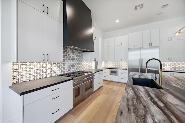 kitchen featuring light wood finished floors, visible vents, high end appliances, wall chimney exhaust hood, and a sink